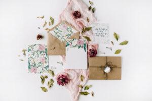 Hochzeitseinladungskarten, Handwerk Umschläge, rosa und roten Rosen und grüne Blätter auf weißem Hintergrund. Draufsicht.