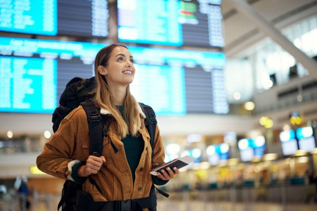 Frau mit Rucksack vor Abflugtafel am Flughafen – Symbol fuer nachhaltiges Reisen mit dem Flughafen Shuttle Frankfurt